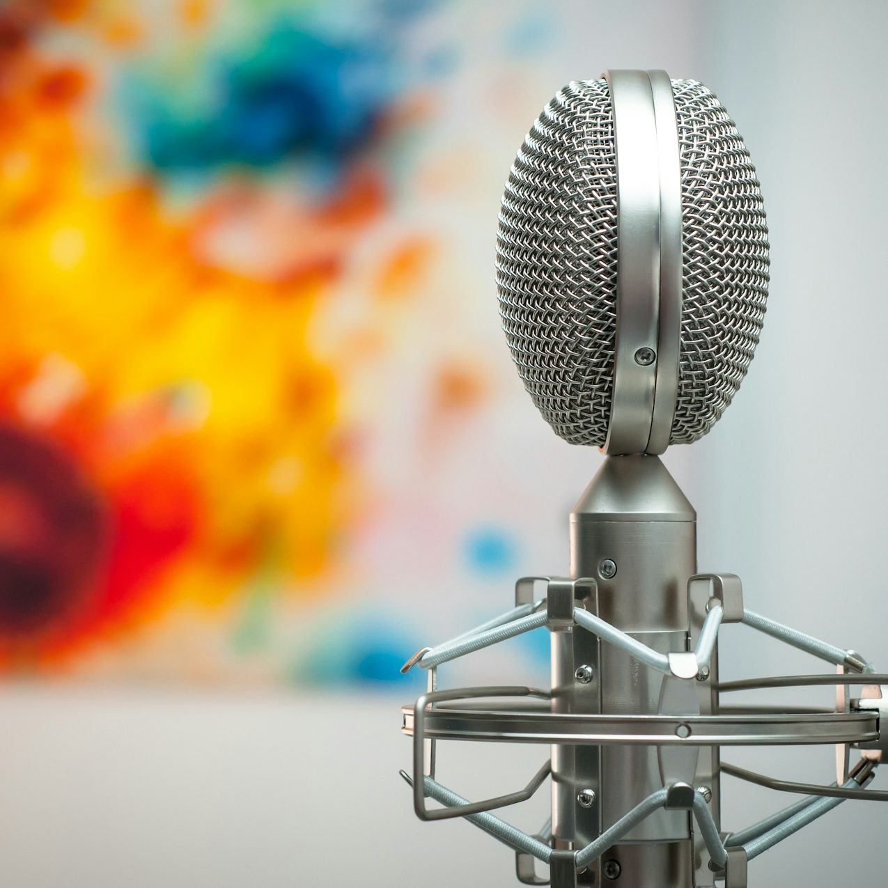 Musikproduktion Mikrofon im Vordergrund, unscharfer bunter Hintergrund mit Farbspritzern.
